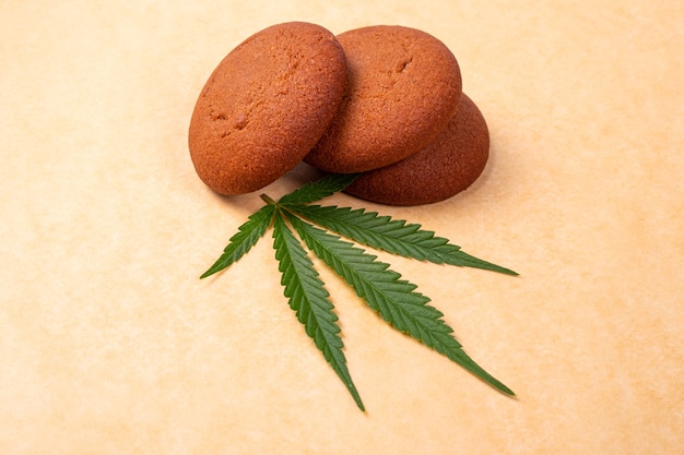 Chocolate chip cookie with green marijuana plant leaf   on a yellow background, sweets with cannabis.