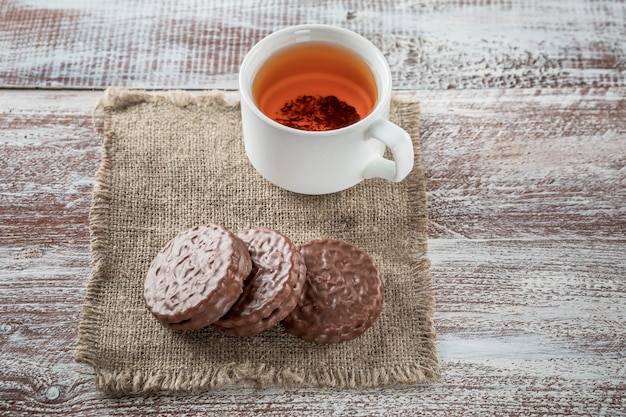 Chocolate chip cookies and a mug of tea on white wooden table.