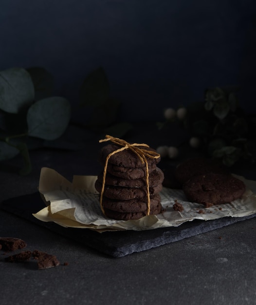 Печенье с шоколадной крошкой, сложенное и перевязанное веревкой, стоит на потертых страницах, лежащих на черном камне