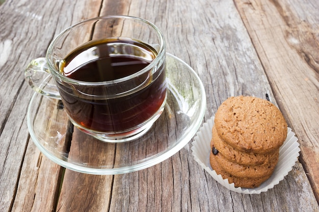 Chocolate chip cookies with a glass of black coffee on wooden table. 