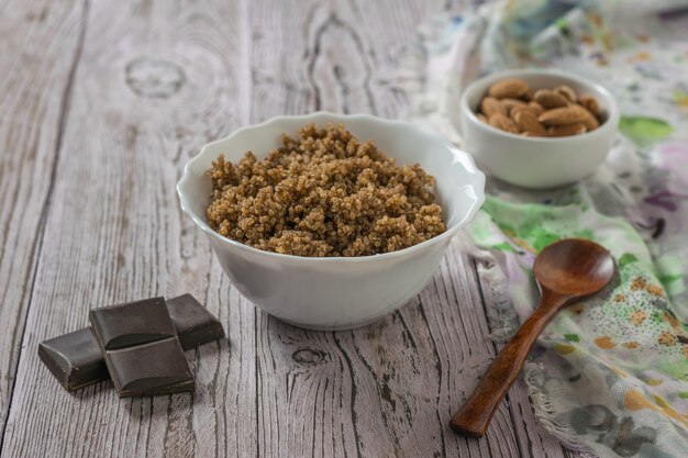 Foto gocce di cioccolato, porridge di quinoa, mandorle e un cucchiaio di legno sul tavolo. dieta sana.