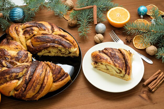 Nonna di natale al cioccolato a forma di ghirlanda con sciroppo d'arancia su un piatto tagliato a pezzi. decorazioni natalizie su un tavolo di legno.