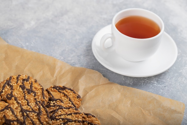 Chocolate coated oatmeal cookies on greaseproof paper with a cup of tea .