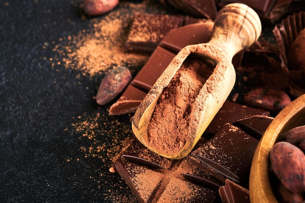 Chocolate and cocoa powder composition of cocoa powder grated\
and bean cocoa bars and pieces of different milk and dark chocolate\
on black background baking chocolate texture top view mock up