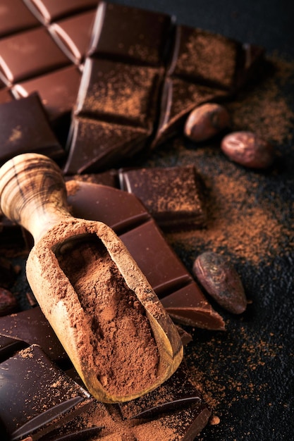 Chocolate and cocoa powder composition of cocoa powder grated
and bean cocoa bars and pieces of different milk and dark chocolate
on black background baking chocolate texture top view mock up