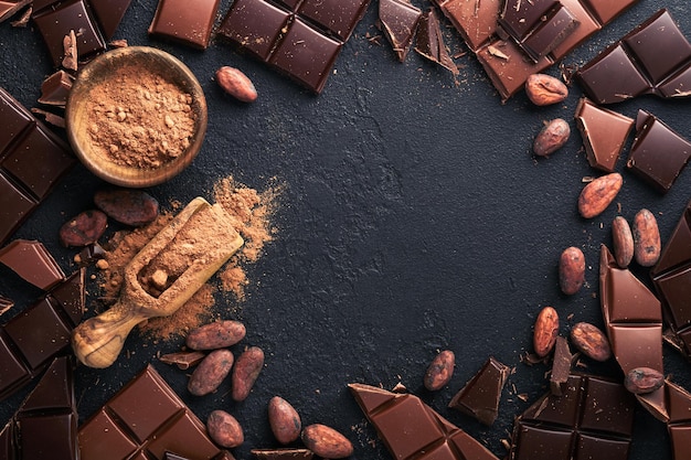 Cioccolato composizione di cacao in polvere grattugiato e barrette di cacao in fagiolo e pezzi di diversi cioccolato al latte e fondente su sfondo nero cottura al cioccolato texture vista dall'alto con spazio di copia mock up