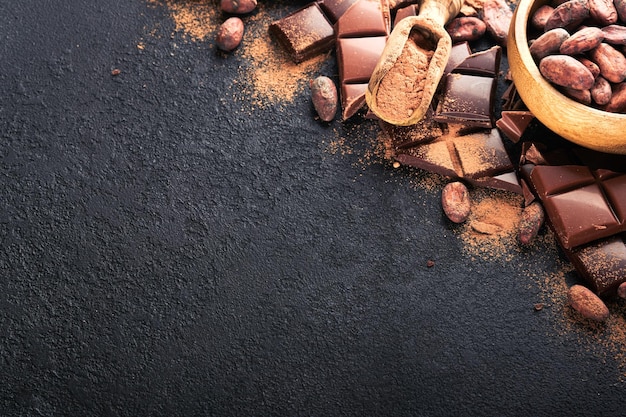 ココアパウダーのすりおろした豆のココアバーと、黒い背景にさまざまなミルクとダークチョコレートの断片のチョコレート組成物ベーキングチョコレートテクスチャコピースペースのある上面図モックアップ