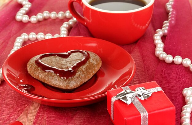 Chocolate cookie in form of heart with cup of coffee on pink tablecloth close-up