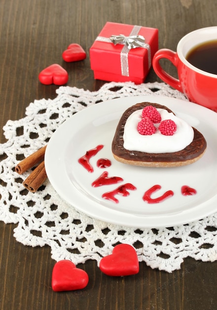 Шоколадное печенье в форме сердца с чашкой кофе на деревянном столе крупным планом
