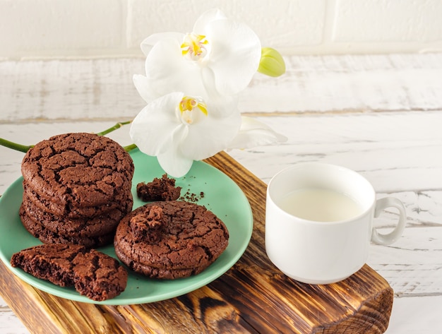 Chocolate cookies for breakfast with a glass of milk on a white wooden table with blloming orchid flower.