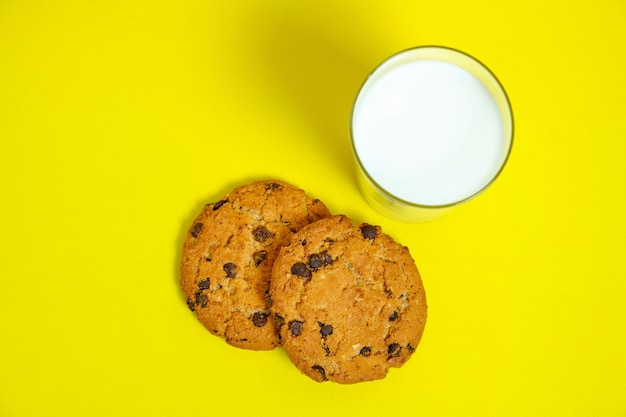 Chocolate cookies and a glass of milk on a bright yellow background, top view.