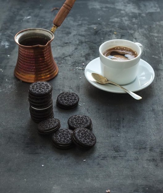 暗いグランジ背景のコーヒーのカップとポットとチョコレートクッキー