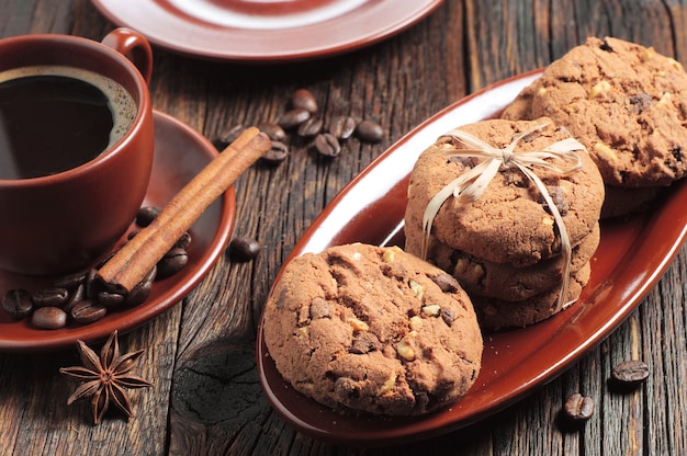 Chocolate cookies with nuts and cup of hot coffee on wooden table. Various brown clayware
