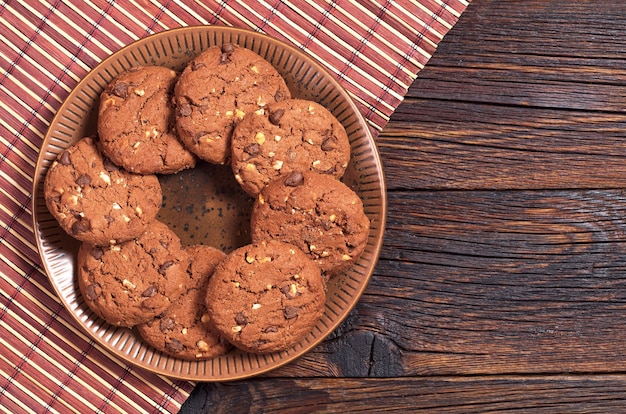 Chocolate cookies with nuts in plate on dark wooden background, top view