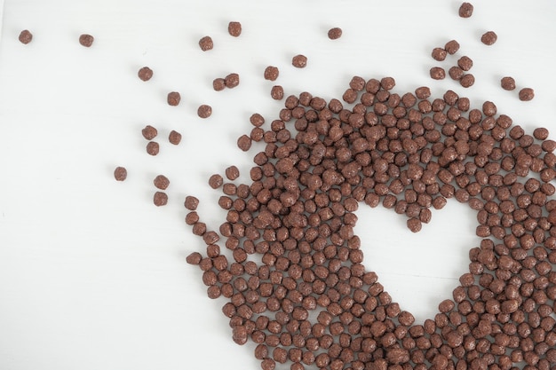 Шоколадные кукурузные шарики разбросаны в форме сердца на белом фоне