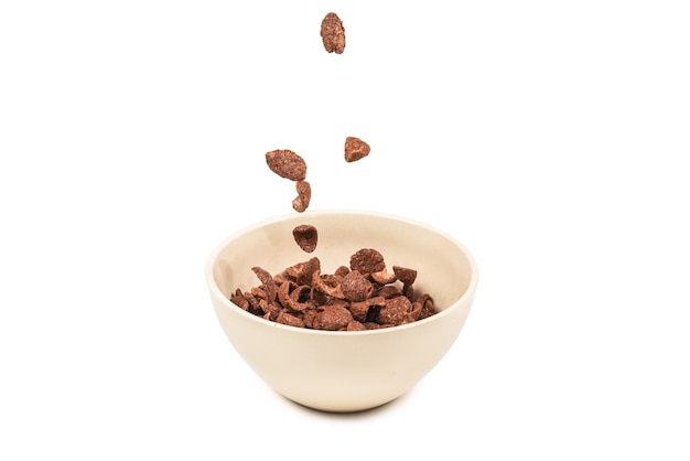 Chocolate corn flakes falling to the white bowl isolated on white. Motion. Copyspace.