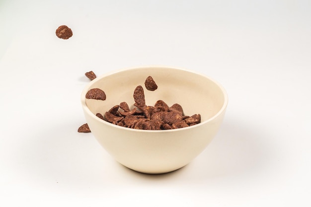 Chocolate corn flakes falling to the white bowl isolated on white. Motion. Copyspace.
