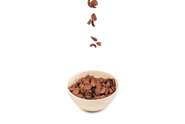 Chocolate corn flakes falling to the white bowl isolated on white. Motion. Copyspace.