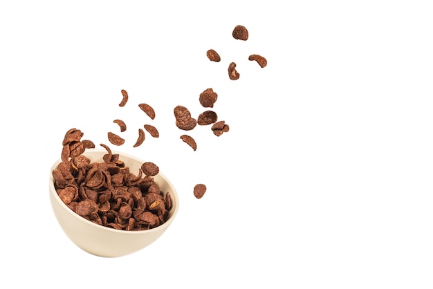 Chocolate corn flakes falling to the white bowl isolated on white. Motion. Copyspace.