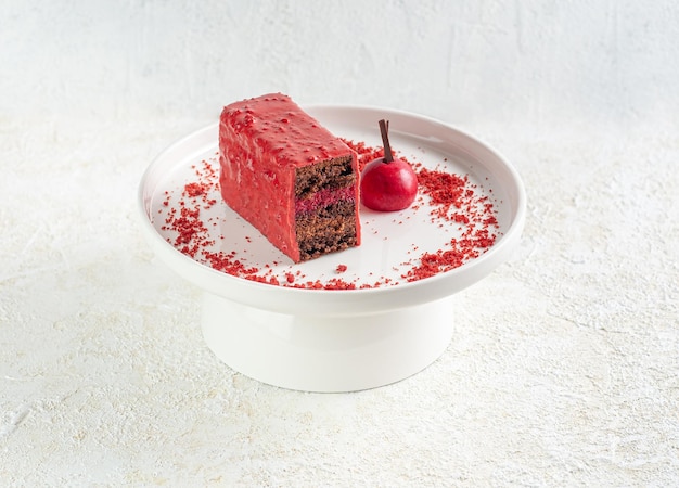 Chocolate covered cherry cake. Sponge cake with a layer of cherry jelly with chocolate mousse. Decorated with crumbs and chocolate. On a white plate. Light background.