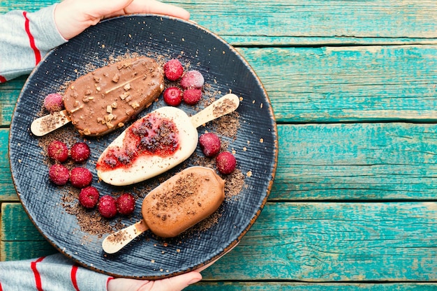 Chocolate covered ice cream with cherry jam on wooden table.Hand holding ice cream