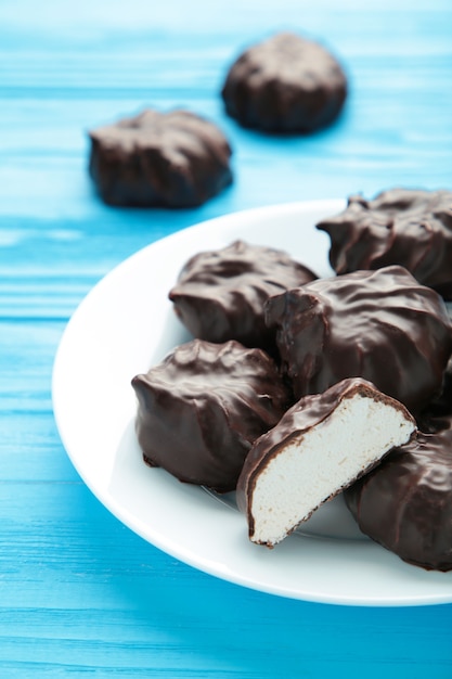 Chocolate covered marshmallows on plate on blue surface