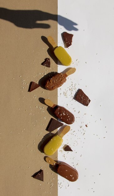 Chocolate and cream ice-cream on sticks with shadow of female hand on white and brown wall