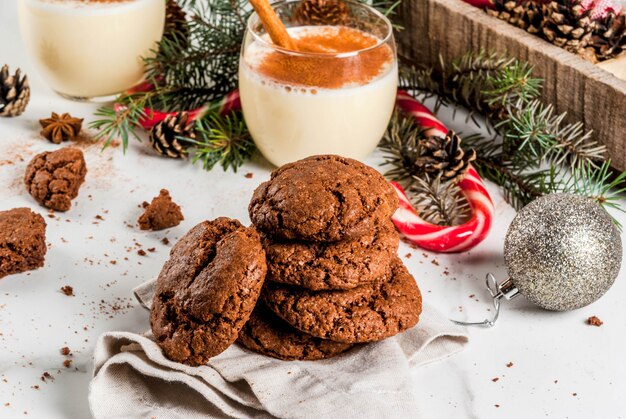 Chocolate Crinkle cookies for Christmas, with eggnog cocktail, candy cane, Christmas tree and holiday decoration, on white marble table