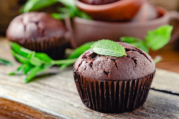 Photo chocolate cupcake muffin with mint leaves in rustic style. fresh baked chocolate muffins with no top on dark wooden background.cupcakes with mint leaf on top.