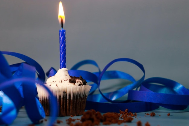 chocolate cupcake with a blue candle, blue background and blue ribbon