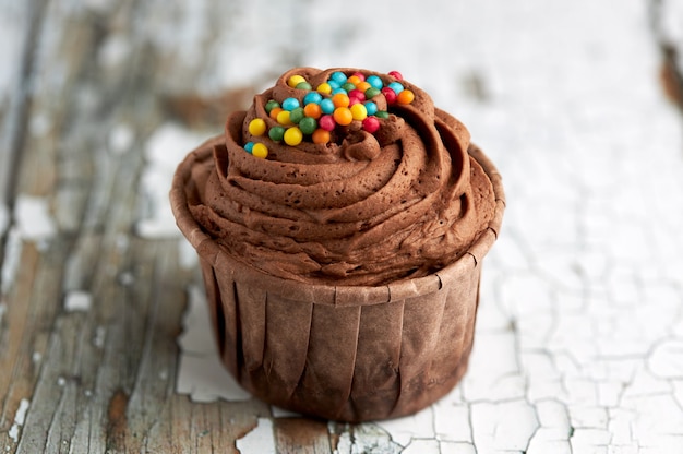 Chocolate cupcake with colorful candies on old wooden table.