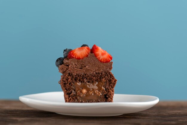 Шоколадный кекс с глазурью из темного шоколада на деревянном столе и синем фоне Шоколадный кекс с карамельной начинкой