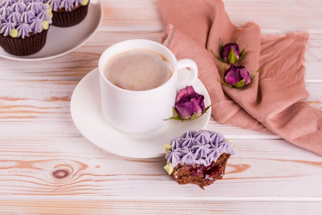 Chocolate delicious cupcake with cream and fragrant coffee with milk on a white wooden table.