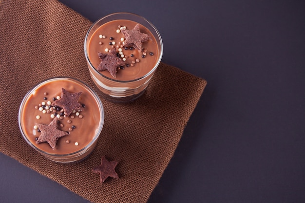 Chocolate dessert in glass jars on a table with wooden spoon. Top view.