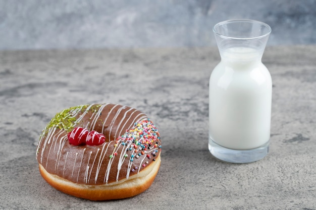 Chocolate donut decorated with sprinkles and glass of fresh milk on stone surface. 