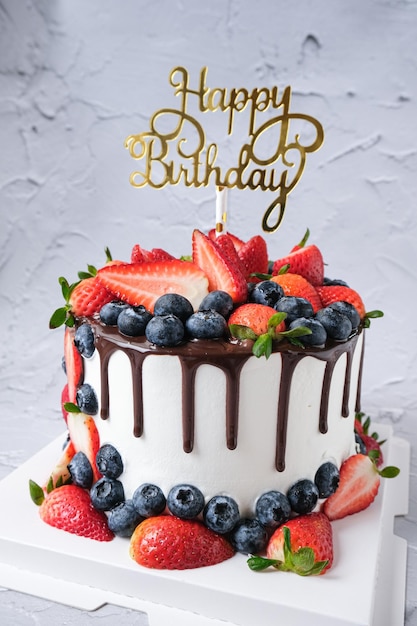 Photo chocolate drip cake with fresh strawberries and blueberries