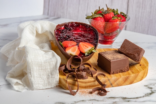 Chocolate Easter egg stuffed with strawberry jam next to blocks and chocolate chips and a bowl of strawberries. Easter scenery.