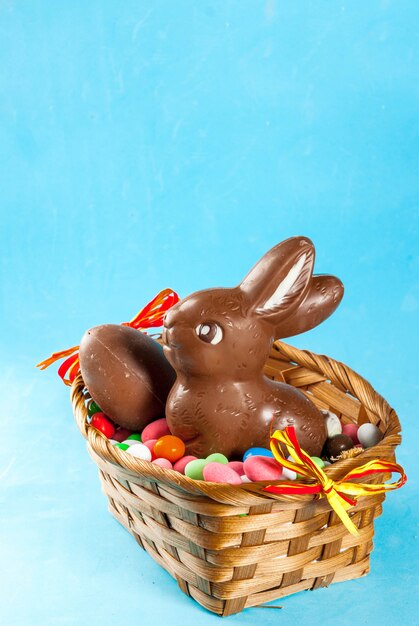 Chocolate easter eggs, bunny and sweets in the basket on light blue surface, easter concept