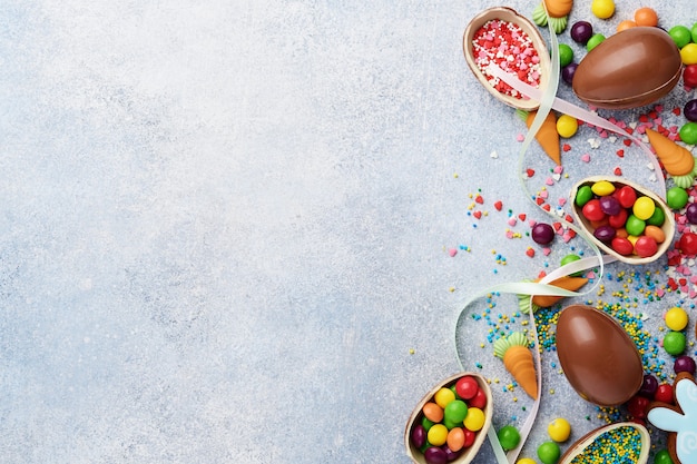 Chocolate easter eggs and colorful sweets on gray table top view. Flat lay with space for your greetings