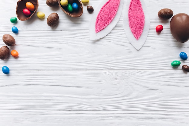 Chocolate Easter eggs and rabbit ears on white wooden background.