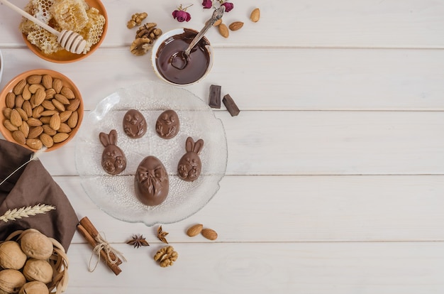 chocolate Easter eggs in the shape of a rabbit and a chicken on a wooden white background with copy space.