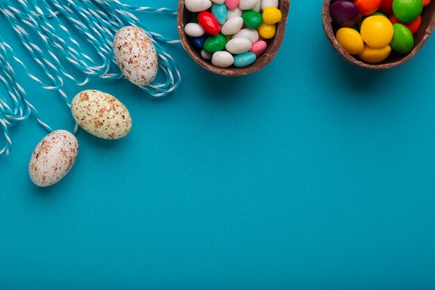 Photo chocolate egg with candies in it and colored quail eggs on a blue background as a symbol of easter f