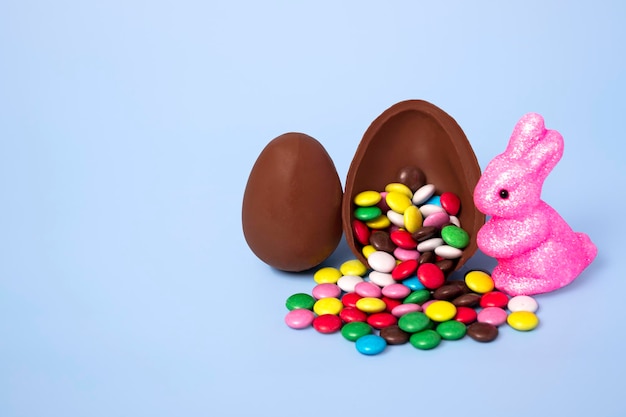 Photo chocolate egg with colorful candies and a rabbit on a blue background festive banner with copy space