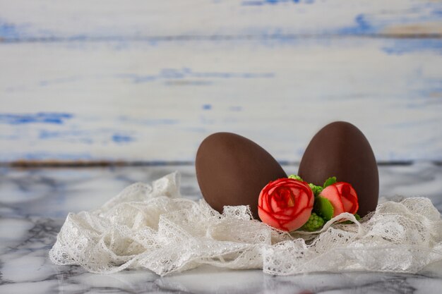 Uova di cioccolato, nastro di pizzo bianco, rose decorative artificiali sulla superficie di legno bianca. concetto di pasqua