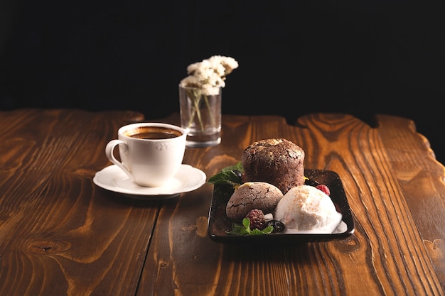 Chocolate fondant with ice cream and berries on a wooden restaurant table next to a cup of coffee