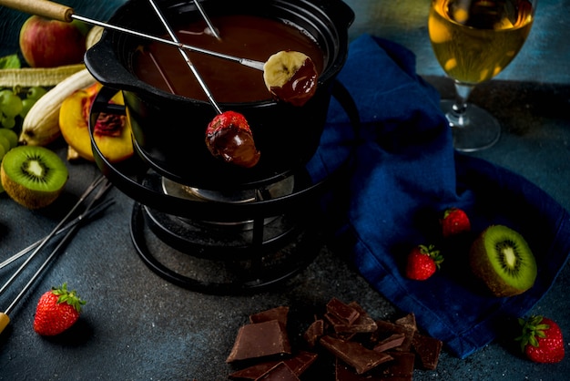 Chocolate fondue in traditional fondue pot, with forks,  white wine, assorted various berries and fruit