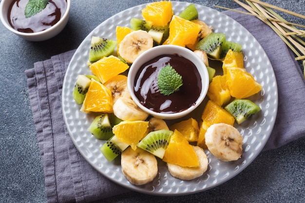 Fonduta di cioccolato con frutta su uno sfondo di cemento scuro. festa estiva di concetto. copia spazio