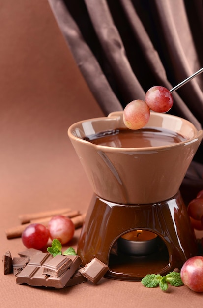 Chocolate fondue with fruits on brown background