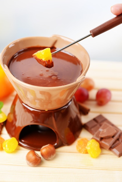Chocolate fondue with fruits on wooden table on light background