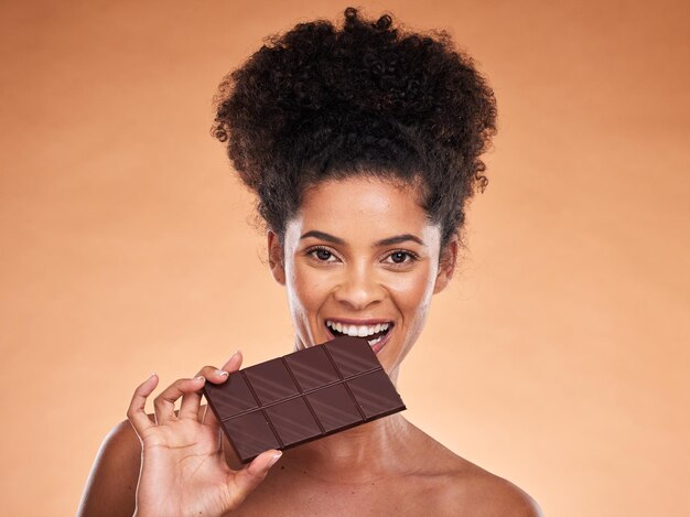초콜릿 행복 한 여자와 아름다움 초상화 스튜디오 배경 및 과자 카카오 디저트를 먹고 설탕을 즐기십시오 흑인 여성은 초콜릿 바 코코아와 사탕 다이어트 칼로리와 스낵 유혹을 물었습니다